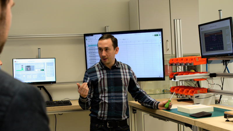 Maxim Reimche stellt den Demonstrator Vernetzung von Produktionsprozessen vor (© Mittelstand 4.0-Kompetenzzentrum Ilmenau) 2 5772 Maxim Reimche stellt den Demonstrator Vernetzung von Produktionsprozessen vor