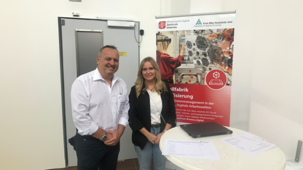 Ein Mann und eine Frau stehen vor einem Banner der Modellfabrik Virtualisierung.