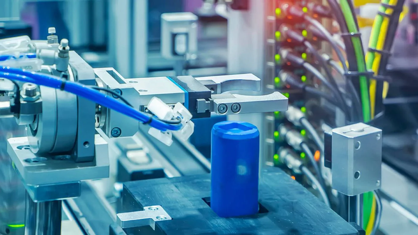 Es ist eine Art Roboter-Arm zu sehen, welcher nach einem blauen Zylinder greift.