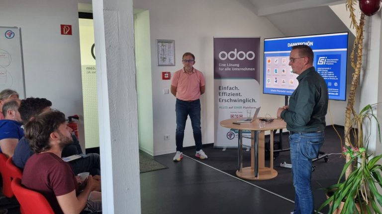 Referenten, ein Bildschirm und sitzend im Vordergrund Gäste