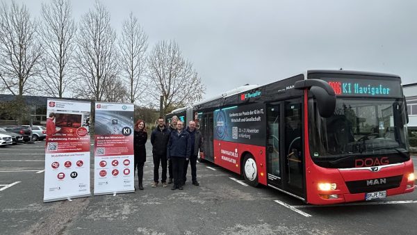 Fünf Personen stehen zwischen zwei Roll-Ups und einem Bus mit der Zielanzeige "DOAG KI-Navigator"