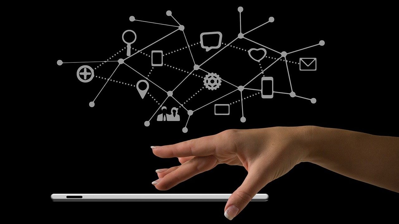 Hand schwebt über einen Tablet und darüber sind verschiedene Icons zu sehen und miteinander verbunden