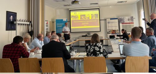 Personen sitzen in einem Raum und schauen auf einen Beamer