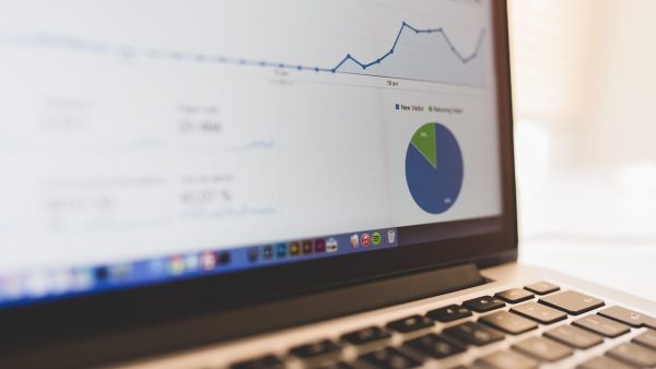 Nahaufnahme eines Laptop-Bildschirms mit Datenanalyse-Dashboard, das ein Liniendiagramm und ein Kreisdiagramm mit den Kategorien ‚New Visitor‘ und ‚Returning Visitor‘ zeigt.
